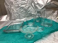 Seven assorted clear glass pieces arranged on blue cloth with aluminum foil background, showing various shapes and sizes.