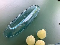 Top view of elongated turquoise glass bowl with three pear-shaped wax candles beside it on a flat surface.