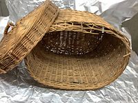 Photo of a large antique wicker basket with lid showing inside and shape, highlighting the woven material and lid.
