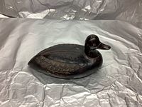 Side view of dark metal duck decoy sculpture showing carved wing detail and wear.