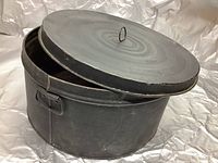 Photo of round metal vintage military hat box with lid off, showing interior and metal loop handle on lid.