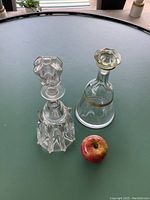 Two glass wine decanters shown upright on a table with an apple for scale; modern conical decanter with gold accents and vintage faceted decanter.