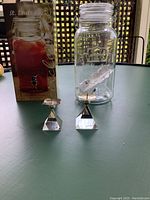 Photo showing the beverage dispenser with its box and two stamped silver candle holders placed on a table