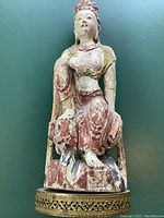 Full front view of the carved statue showing the figure seated on a carved base with painted details in red, green and gold.