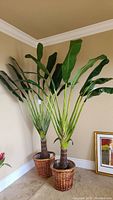 Two artificial banana palm trees with green leaves and wicker basket bases, positioned in a corner.