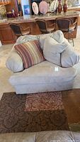 Front view of large suede chair with light beige upholstery and two throw pillows, positioned on area rugs.