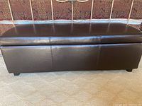 Front view of a rectangular dark brown leather foot chest with cushioned top and four short feet