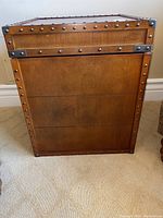 Wooden chest from front view showing metal stud accents on edges and wood grain surface.