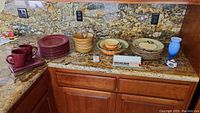 Full view of ceramic dishware sets including mugs, plates, bowls, chopsticks, and decorative vases on granite countertop.