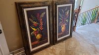 Two large framed floral paintings leaning against a wall with railing visible in background