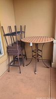 Photo showing four brown woven high stools stacked and the round wooden slatted highball table with metal legs.