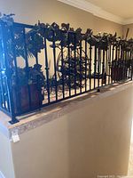 Wide view showing multiple faux plants with green leaves in urn-like containers arranged along a black wrought iron railing decorated with faux ivy.