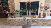 Full view of vases and horse figurine displayed on a stone mantel surrounding a fireplace. Various vase materials include wicker, wood, glass, and metal. Horse figurine on wooden base in front.