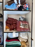 Photo of white shelving with various folded bath towels, blankets, and linens in multiple colors including brown, blue, burgundy, beige, teal and striped towel