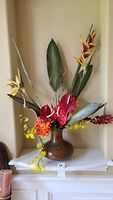 Full view of metal vase with floral faux arrangement showing various colorful flowers and green leaves.