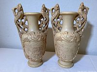 Front view of the two carved vases showing intricate bird and branch handles and detailed carved scenes on the bodies.