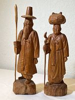 Front view of the pair of carved wood Chinese figurines, showing the man with a tall hat and staff, and the woman with an object on her head and cane.