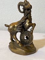 Front and side view of brass goat figurine atop ancient Chinese coin replicas, showing detailed features and coin characters.