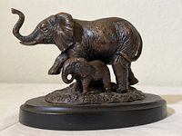 Side view of bronze elephant mother and baby sculpture on wood base showing detailed textures and raised trunk of adult elephant.