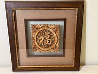 Framed wooden carving of Chinese happiness symbol with beige mat and dark wood frame, front view.