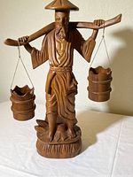 Full view of the wooden statue showing the entire figure and buckets hanging from yoke.