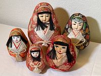 Five Japanese Daruma cloth figures in various sizes and colorful traditional kimono textiles, arranged on a flat surface.