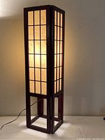 Full view of the lamp showing the dark wooden grid frame and illuminated paper shade with natural fibers.