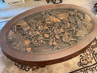 Top-down view of the oval coffee table showing the carved samurai battle relief under the glass top