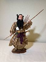 Full front view of samurai figurine standing on a wooden base, holding staff and with arrows on back.