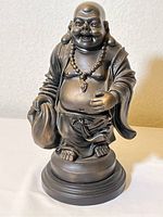 Front view of the figurine showing the Laughing Buddha smiling, holding a sack, wearing a beaded necklace and robe.