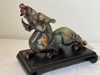 Side view of stone Fu Dog sculpture showing open mouth, detailed carving, and placement on wooden stand.