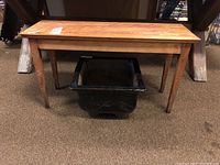 Photo showing wood bench with scratches and stains, positioned above the black ceramic planter, showing bench's tapered legs and rectangular seat surface.