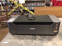 Front view of Canon black inkjet printer on table with power cord on top.