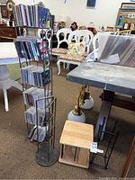 Tall rotating metal CD rack filled with many CDs in jewel cases, standing upright in an indoor setting.