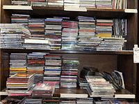 Large assortment of CDs stacked on shelves and a surface, varying genres visible