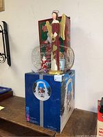 Overview of lot showing glass angel figurine, clear glass platter, and boxed Holiday Ice glass sculpture on a large blue box base, with a smaller Santa figurine in front.