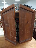 Front view of wooden dart board cabinet with closed doors showing wear and scratches.