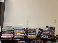 Photo of multiple stacks of DVDs on a shelf and table, titles include children's movies, musicals, and others.