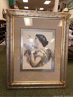 Full front photo of framed lithograph showing woman in profile holding flowers, gold frame, beige mat