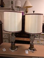 Two matching 32 inch lamps with etched frosted glass bodies, metal and stone bases, cream cylindrical shades with maroon trim, standing on a table
