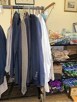 Photo showing multiple men's suit jackets and dress shirts on hangers, hung on a metal rack in a storage area.