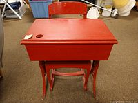 Red vintage school desk with matching chair showing wear, scratches, and chips in paint, front view