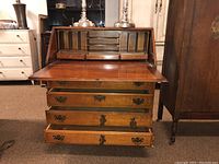 Secretary desk opened, showing writing surface, 3 small drawers, and cubbies inside the top compartment plus 4 drawers below, one drawer pull hanging.