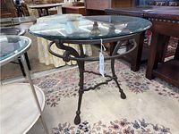 Angle showing the wrought iron base with rounded feet and decorative curved elements under the glass top, on a patterned rug.