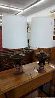 Two table lamps shown side by side on wooden table with wood and smoked glass bases and white fabric shades.