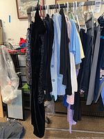 Photo of women's clothing on a rack showing variety of blazers, tops, sweaters, pants in multiple colors including black velvet garment