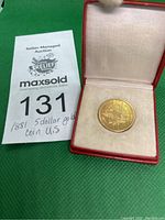 Coin in open red case showing coin seated on white interior alongside lot tag