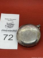 Top view of antique pocket watch showing engraved design on metal case and winding loop.