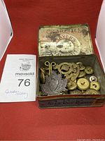 Cigarette tin filled with assorted Canadian military buttons and a pin, showing the lot and container.