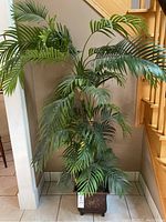 Full view of the artificial palm plant standing beside a staircase on tiled floor.